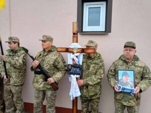 Прощання з полеглим. У руках військових:  хрест, портрет,, прапор