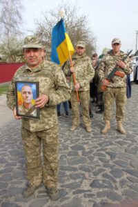 Прощальна церемонія. Попереду У руках військових портрет героя, прапор, автомат