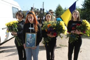 Попереду молоді односельці з квітами, портрет, прапор