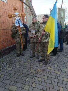 Попереду військові. У руках хрест, портрет, прапор 