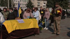 Прощання. Домовина застелена жовто-блакитним прапором. Рушник, хліб
