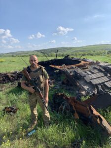 Володимир, озброєний у повний зріст на фоні розбитого танка
