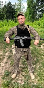 Данілов у аовний зріст з автоматом. На фоні зелених дерев